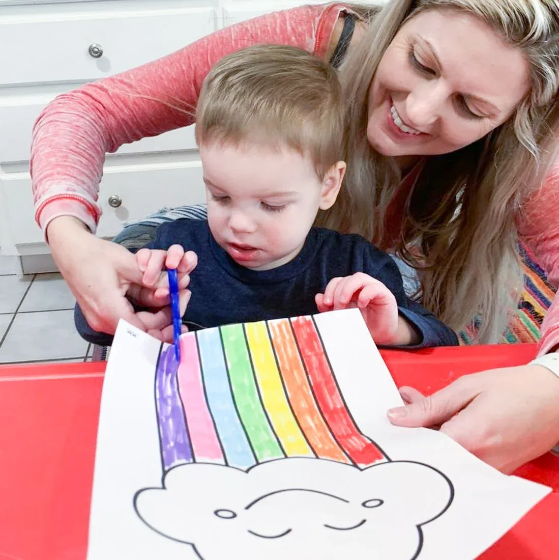 A teacher helping a child cut paper at a red table
