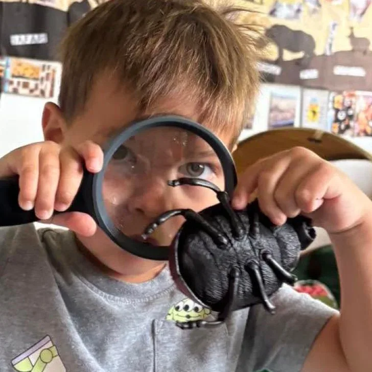 Child examining a toy spider through a magnifying glass