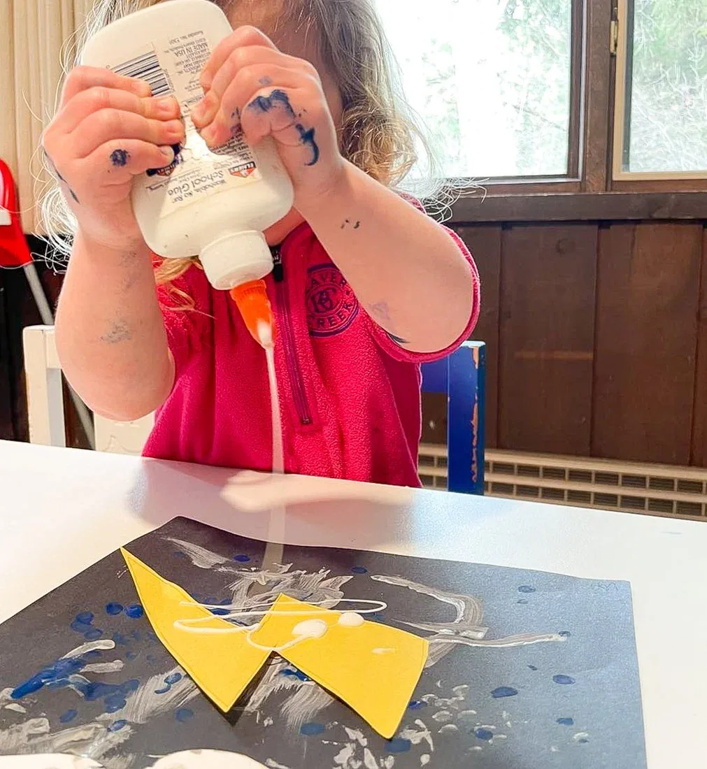 A child squeezing glue onto a paper craft