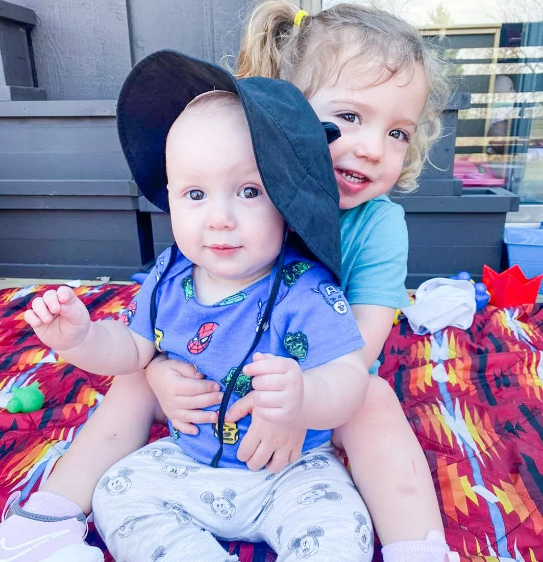 An older child sitting behind a younger child on a porch